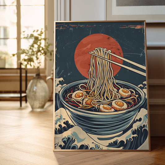 A framed art print depicting a bowl of ramen with chopsticks lifting noodles, set against a Japanese wave background and a large red sun, displayed on a wooden floor in a softly lit room.