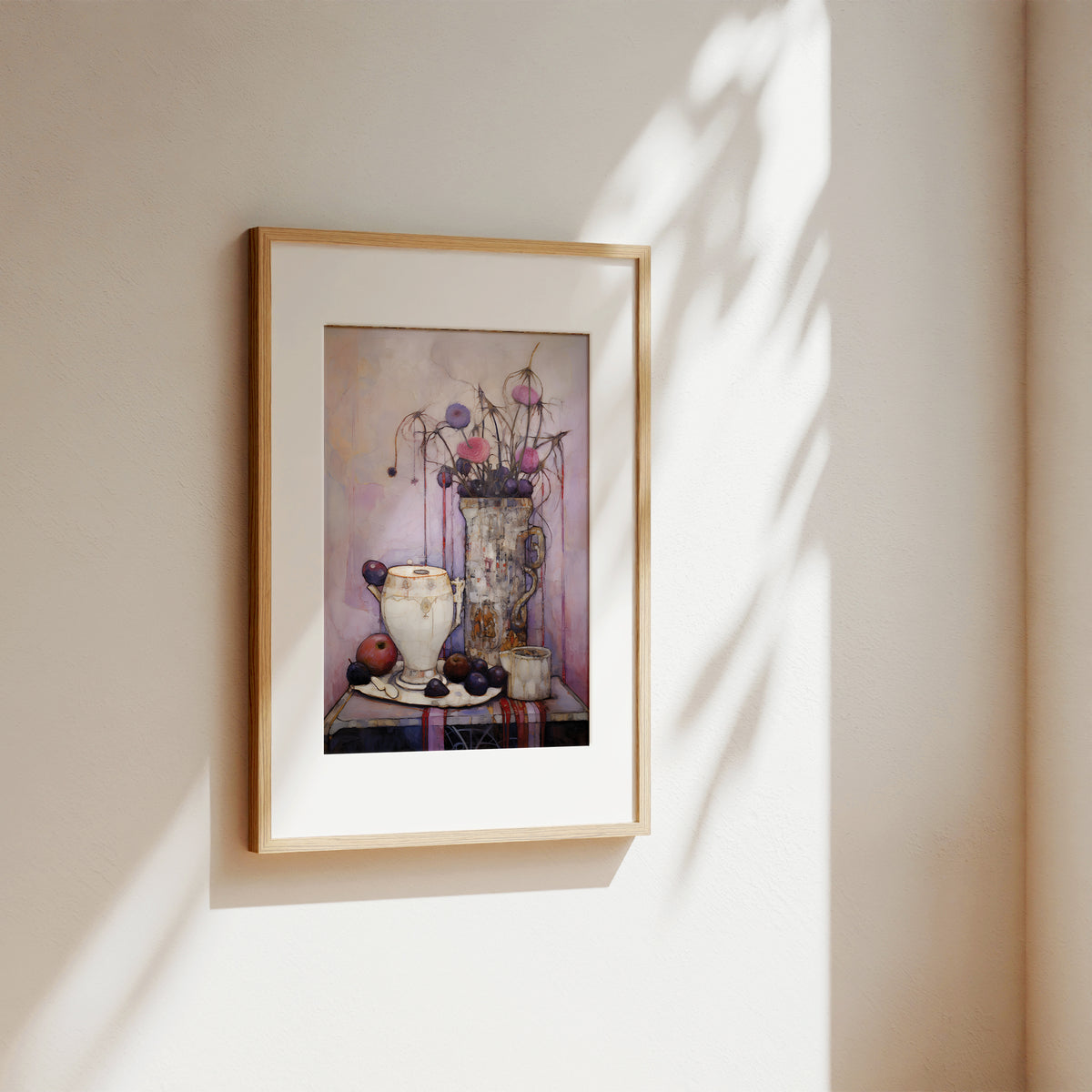 A framed still life art print hanging on a beige wall, featuring a vase with dried flowers and fruit in muted pink, purple, and cream tones. The frame is light wood with a white mat, photographed in soft natural light with leaf shadows cast across the wall.