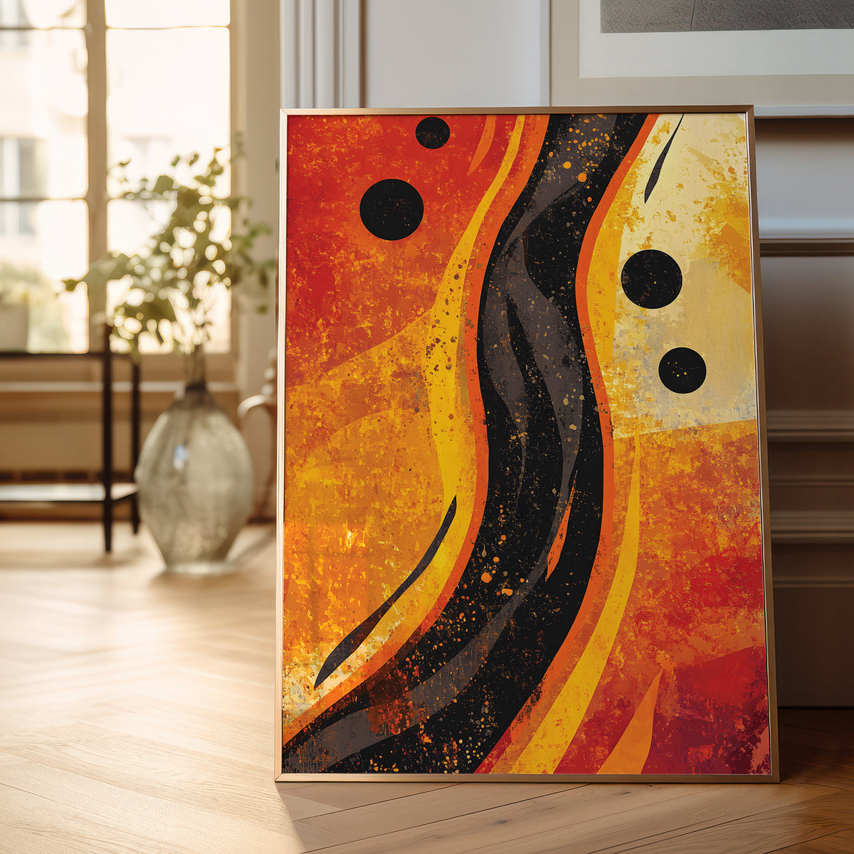 A framed abstract canvas print with bold wavy lines in orange, yellow, black, and red, leaning against a wall on a light wood floor in a bright, modern room.
