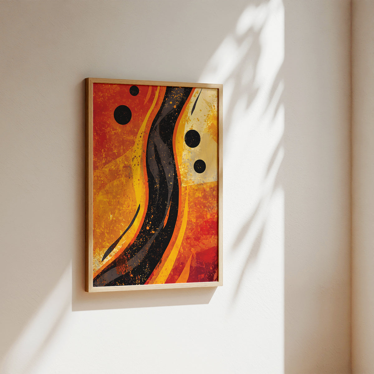 Abstract framed wall art hanging on a warm off-white wall, with sunlight casting leaf shadows across the artwork and wall. The painting features flowing orange, red, yellow, and black abstract shapes with black circular dots.