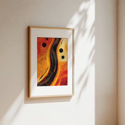 Framed abstract wall art hanging on a warm beige wall, with sunlight casting leaf-like shadows across the surface. The artwork features swirling orange, red, yellow, and black abstract forms with black circular accents, set in a light wood frame with a white mat.