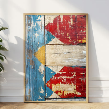 A framed wall art print featuring a distressed, weathered design inspired by the Philippine flag, with peeling blue, red, yellow, and off-white wood textures, displayed leaning against a white wall.