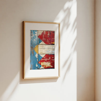 Framed wall art hanging on a beige wall, featuring an abstract rustic design with red, blue, white, and yellow distressed wood textures. The piece is enclosed in a light natural wood frame with a white mat, casting soft shadows on the wall.