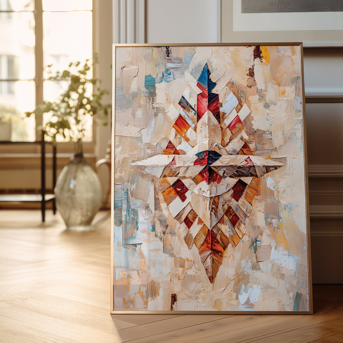 A framed abstract canvas painting with a geometric star-like composition in cream, beige, orange, red, blue, and brown tones, leaning against a wall on a light wood floor in a softly lit interior.