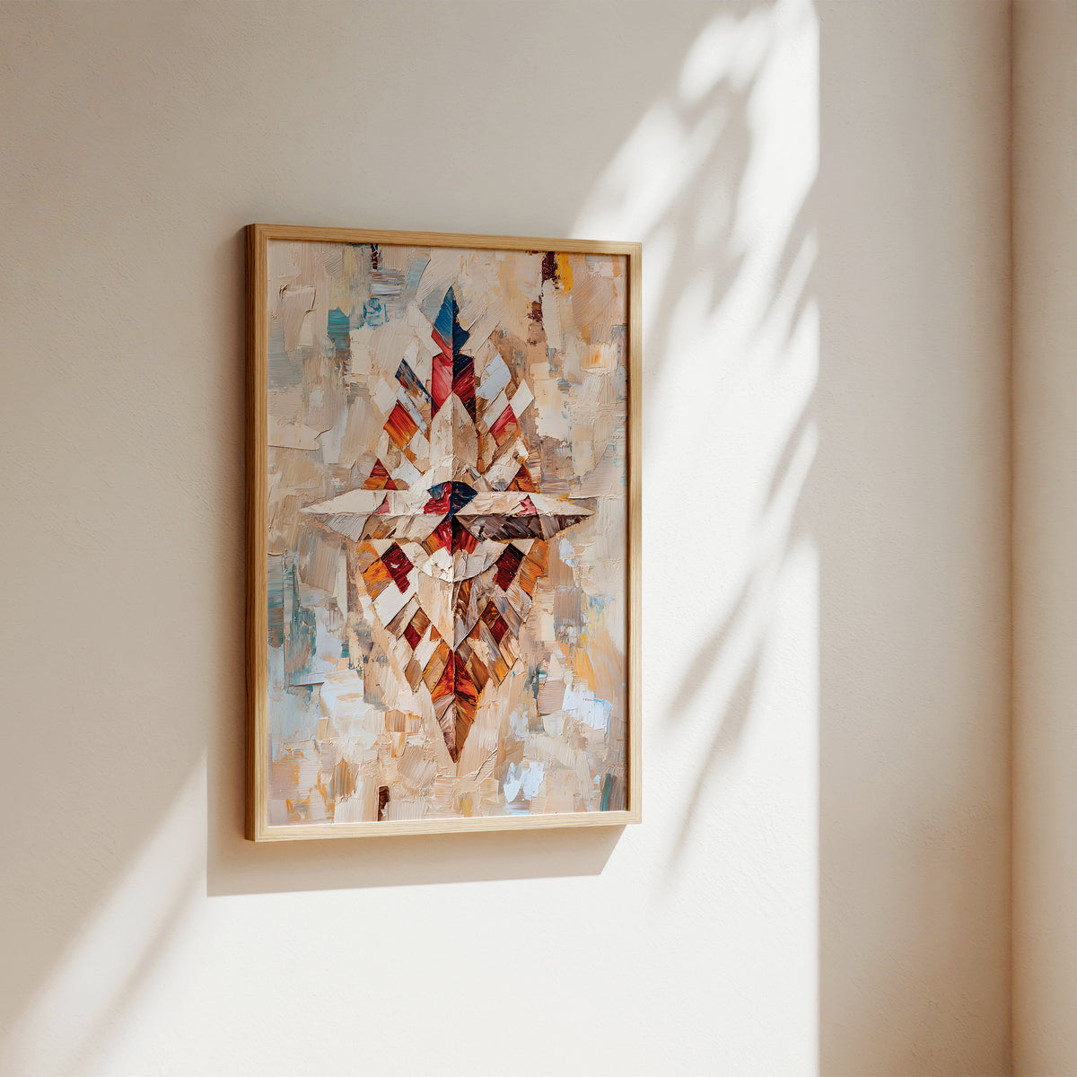 A framed abstract geometric wall art print hangs on a warm beige wall, with soft sunlight casting leafy shadows across the surface. The artwork features a central diamond-like emblem in red, brown, cream, and blue tones, enclosed in a light wood frame.