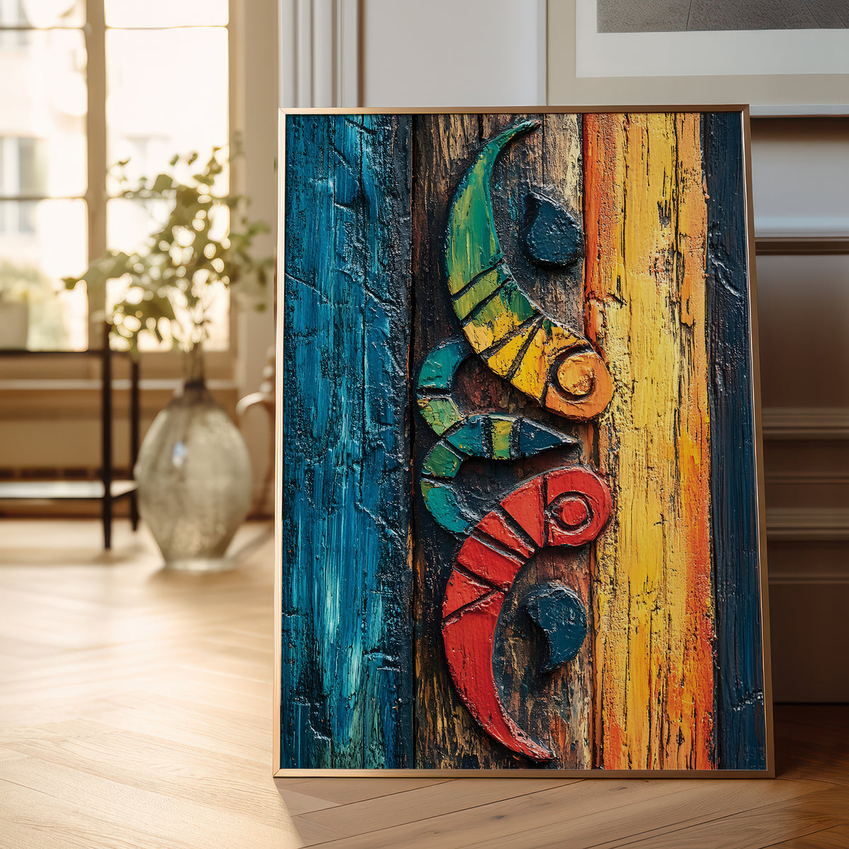 A framed abstract art print featuring a stylized floral ornament in bold red, yellow, blue, black, and white brushstrokes, leaning against a white wall on a light wood floor with a plant visible at the left edge.