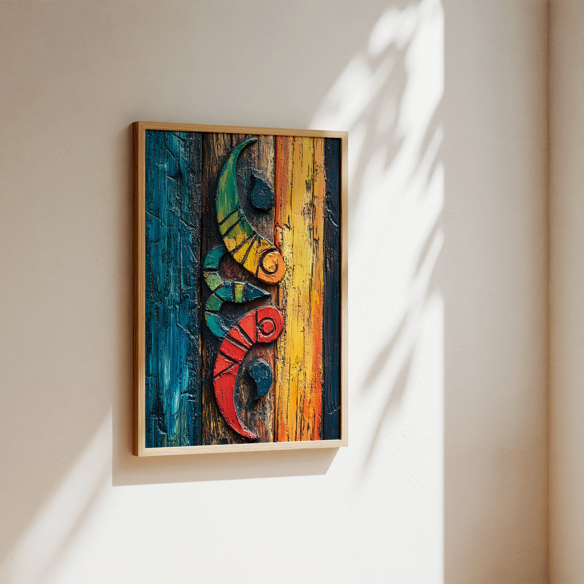 A framed abstract art print featuring a stylized floral ornament in bold red, yellow, blue, black, and white brushstrokes, leaning against a white wall on a light wood floor with a plant visible at the left edge.
