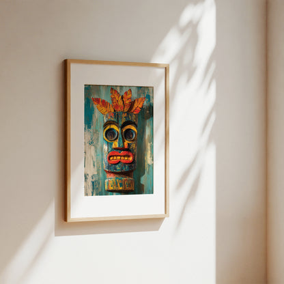A framed art print featuring a colorful tiki mask on a textured teal background, hanging on a warm beige wall with soft leaf shadows cast across it.