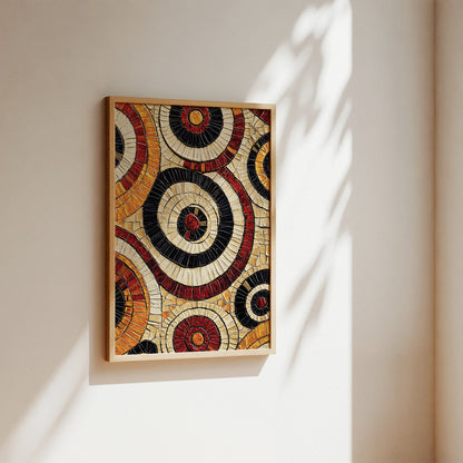 A framed circular mosaic wall art piece with concentric rings in cream, black, red, and orange, hanging on a warm beige wall with soft sunlight and leaf shadows.