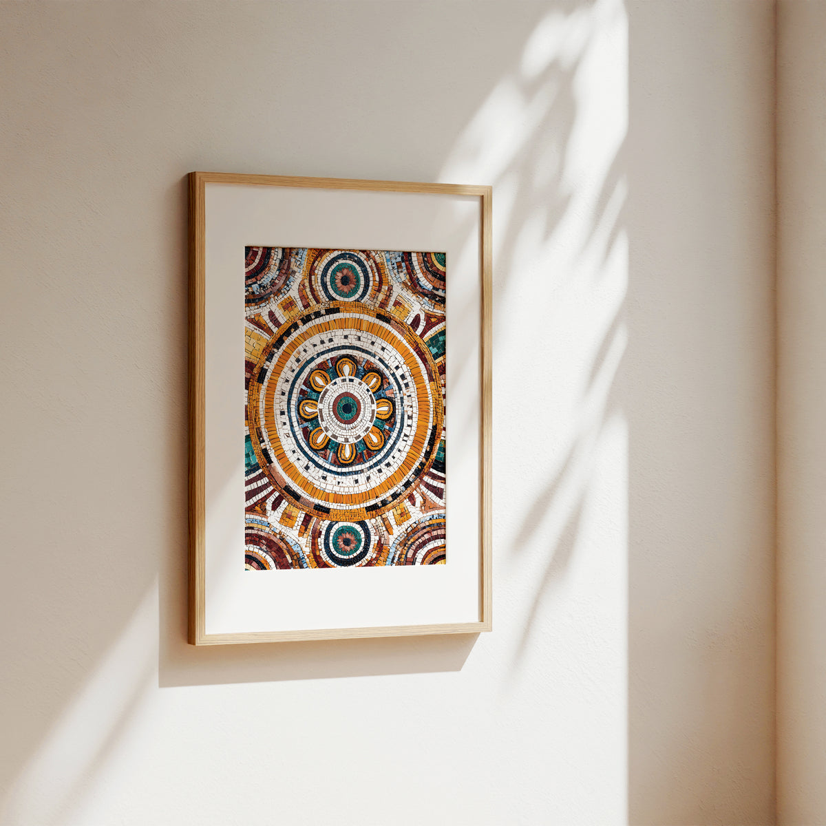 A framed art print featuring a detailed, colorful circular mandala design, hanging on a warm beige wall with soft sunlight and leaf shadows cast across it.