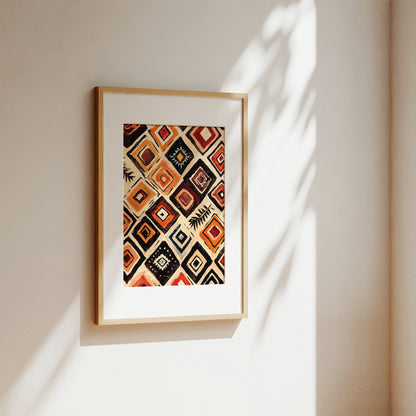 Framed geometric art print with a Southwestern diamond pattern in orange, red, black, and beige, displayed on a warm beige wall with soft leaf shadows.