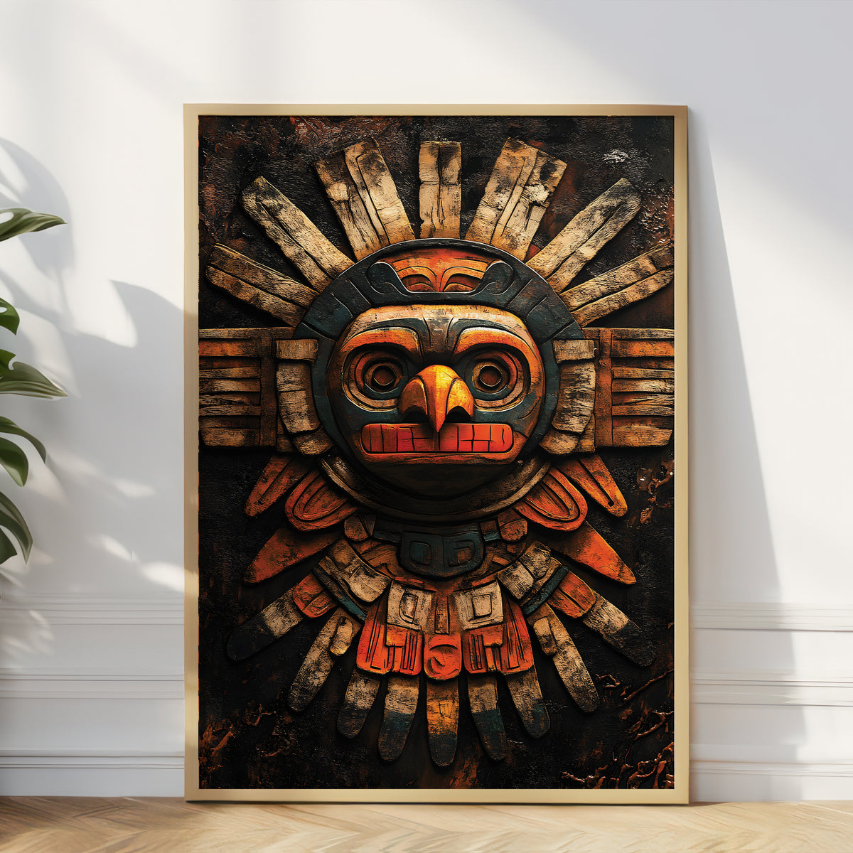 A framed art print featuring a stylized, weathered Aztec-inspired sun mask with orange, red, and black details on a dark background, leaning against a white wall on a light wood floor.