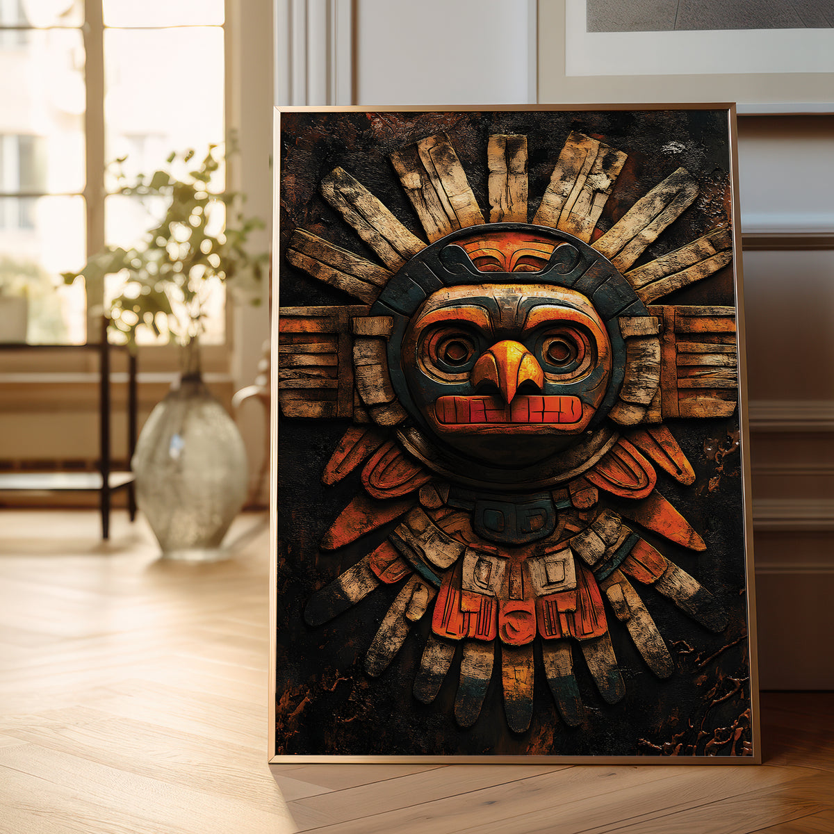 A framed art print featuring a stylized, multi-dimensional wooden Aztec sun god mask, leaning against a wall on a light wood floor in a bright, modern room.
