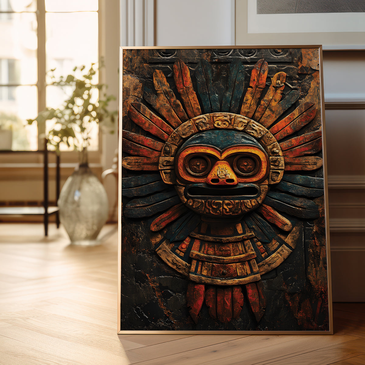 A framed vertical art print featuring a detailed Aztec-style calendar mask with a sunburst design, leaning against a wall on a light wood floor in a softly lit room.