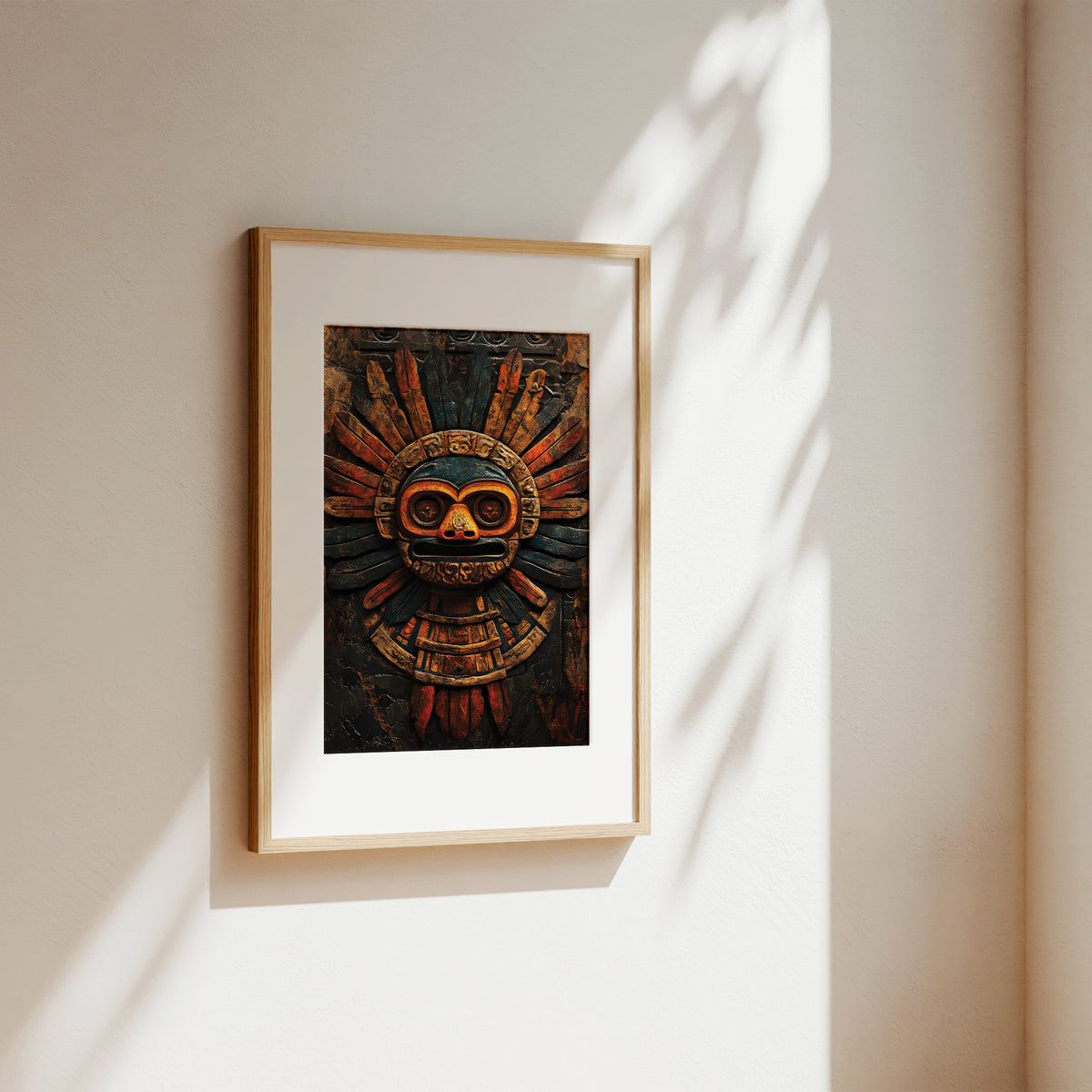 A framed art print featuring an Aztec calendar skull design, displayed on a warm beige wall with soft, dappled sunlight casting leaf shadows.