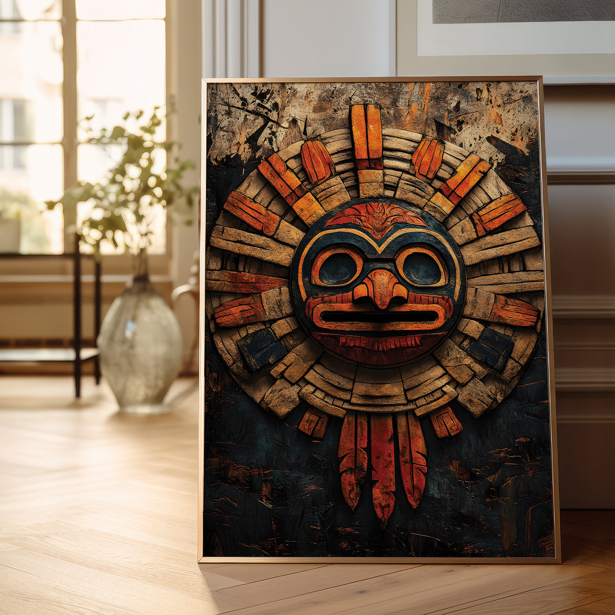 A framed art print featuring a stylized Aztec-inspired sun mask, leaning against a wall on a light wood floor in a bright, modern room.