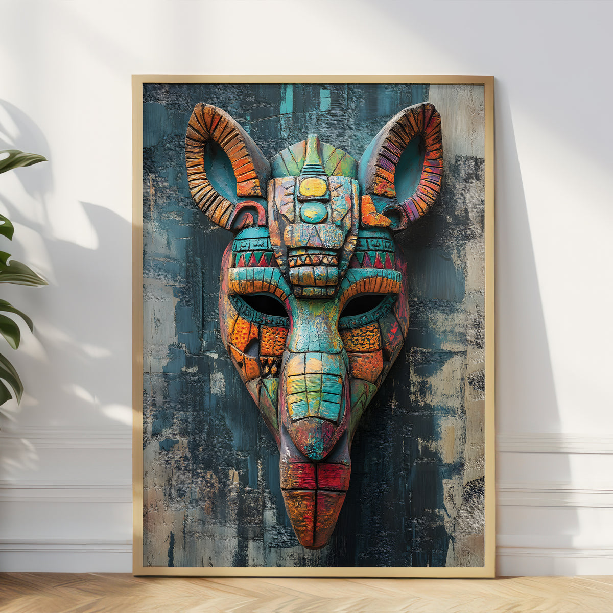 A framed wall art print featuring a colorful stylized ram or goat head mask with geometric patterns, leaning against a white wall on a light wood floor. The artwork contains teal, orange, red, yellow, and blue tones, and the frame is light wood.