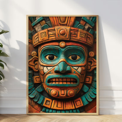 A framed art print featuring a detailed Aztec-style carved face mask in vibrant turquoise and terracotta orange, leaning against a white wall on a light wood floor next to a green plant.