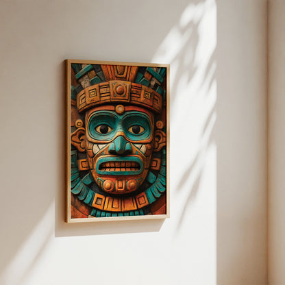 A framed art print featuring a detailed Aztec-style mask in vibrant turquoise, orange, and brown tones, hanging on a warm beige wall with soft sunlight and leaf shadows.