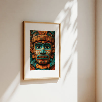 A framed art print featuring a detailed Aztec-style face mask in teal, gold, and brown tones, displayed on a warm beige wall with soft sunlight and leaf shadows.