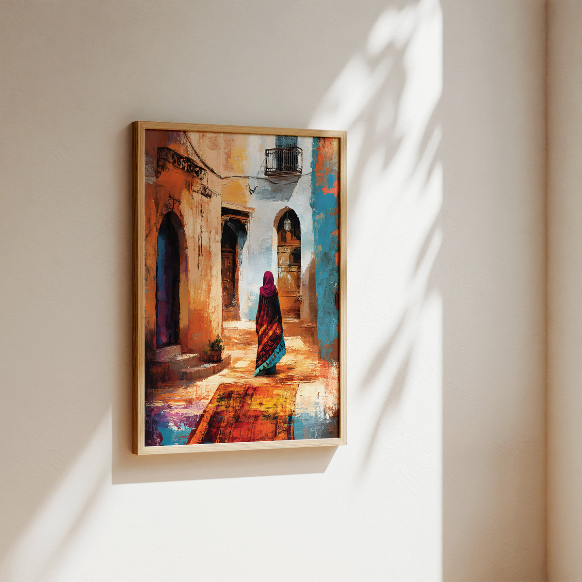 A framed painting of a woman in a colorful sari walking down a sunlit alleyway with arches and warm-toned buildings, displayed on a beige wall with soft shadow patterns.