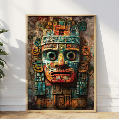 A framed vertical art print featuring a stylized Aztec-inspired face mask in rich teal, rust red, ochre, and brown tones, leaning against a white wall on a light wood floor with a plant partially visible at the left edge.