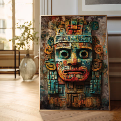 A framed art print featuring a stylized Aztec-style mask with teal, rust red, and gold tones, leaning against a wall on a light wood floor in a softly lit room.