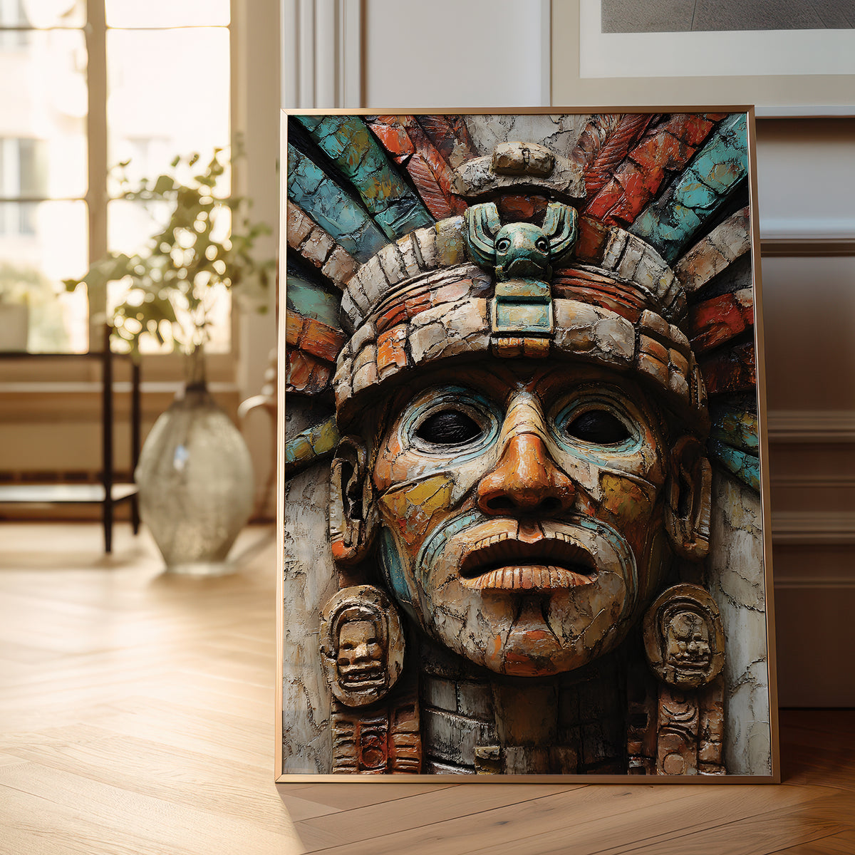 A framed art print featuring a detailed, colorful Aztec-style face mask with a headdress, leaning against a wall on a light wood floor in a modern room setting.