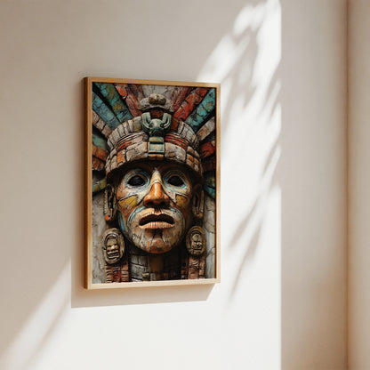 A framed art print featuring an Aztec-style warrior face sculpture, hanging on a warm beige wall with soft sunlight and leaf shadows cast across it.