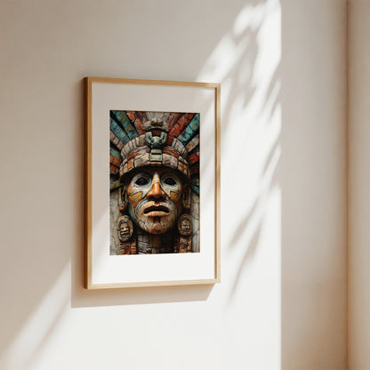 A framed art print featuring a detailed Aztec-style mask with a colorful feathered headdress, displayed on a warm beige wall with soft, dappled sunlight and leaf shadows.