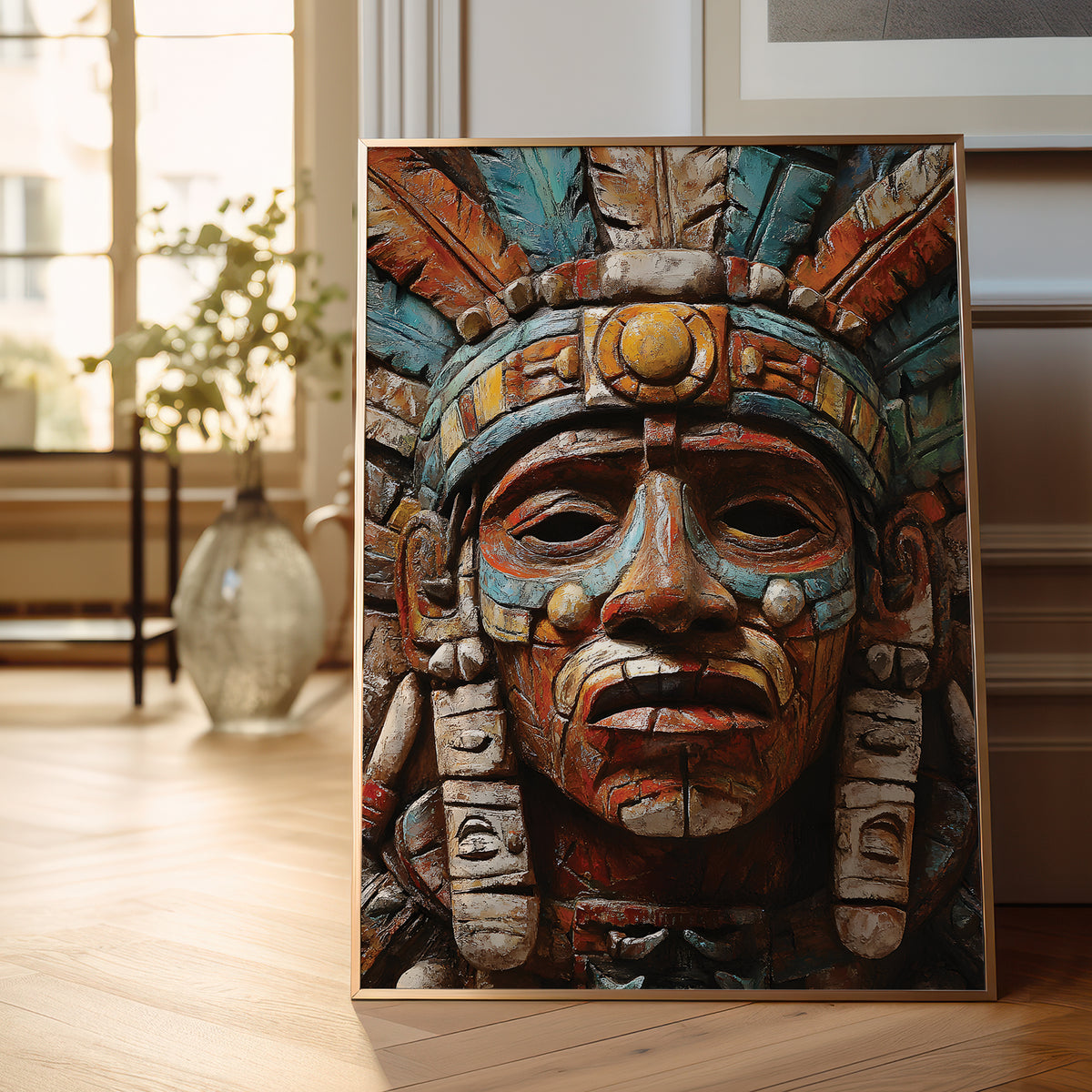 A framed vertical canvas print of a detailed Aztec-style warrior head sculpture with turquoise, gold, and brown tones, leaning against a wall on a light wood floor in a bright room.