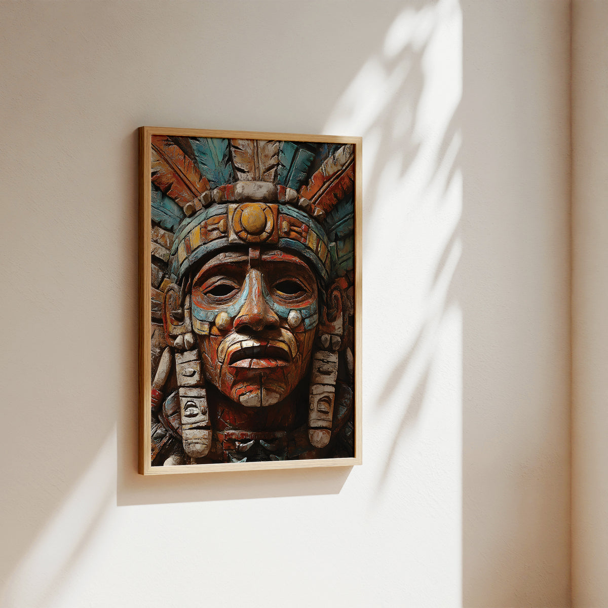A framed art print featuring a detailed Aztec-style warrior head carving, displayed on a warm beige wall with soft sunlight and leaf shadows.