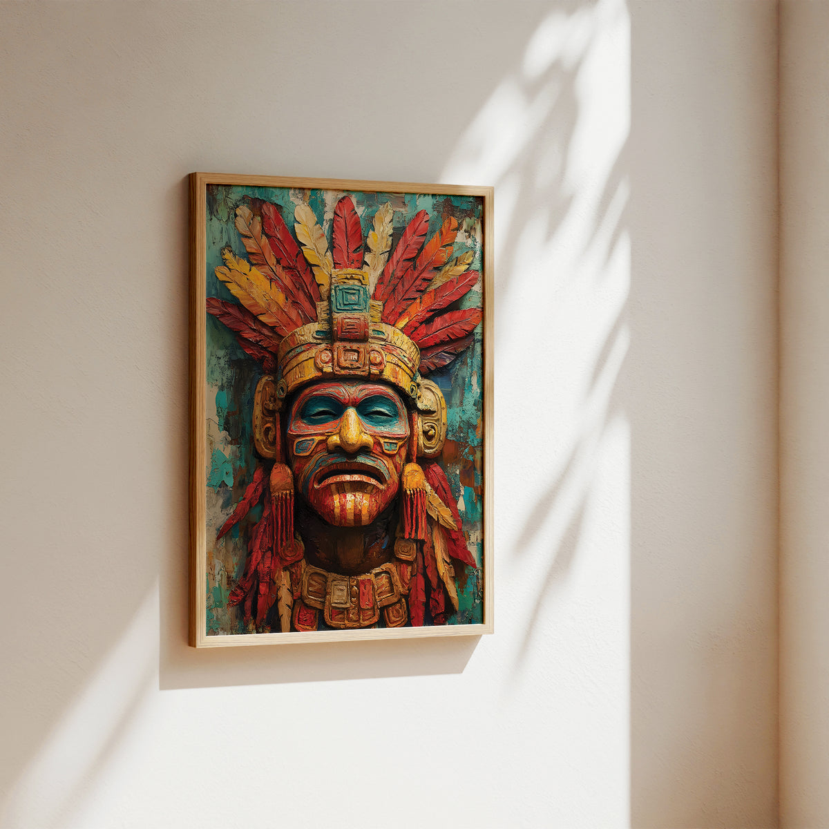 A framed art print depicting a detailed Aztec-style warrior head with a red and gold feathered headdress, mounted on a warm beige wall with soft sunlight and leaf shadows.