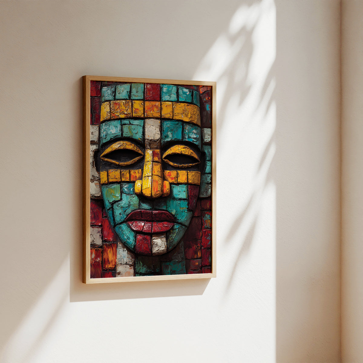 A framed mosaic wall art print depicting a stylized face made of colorful geometric tiles, hanging on a beige wall with soft sunlight and leaf shadows.