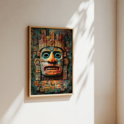A framed art print featuring a detailed Aztec-style face mask with intricate geometric patterns, hanging on a warm beige wall with soft sunlight and leaf shadows.
