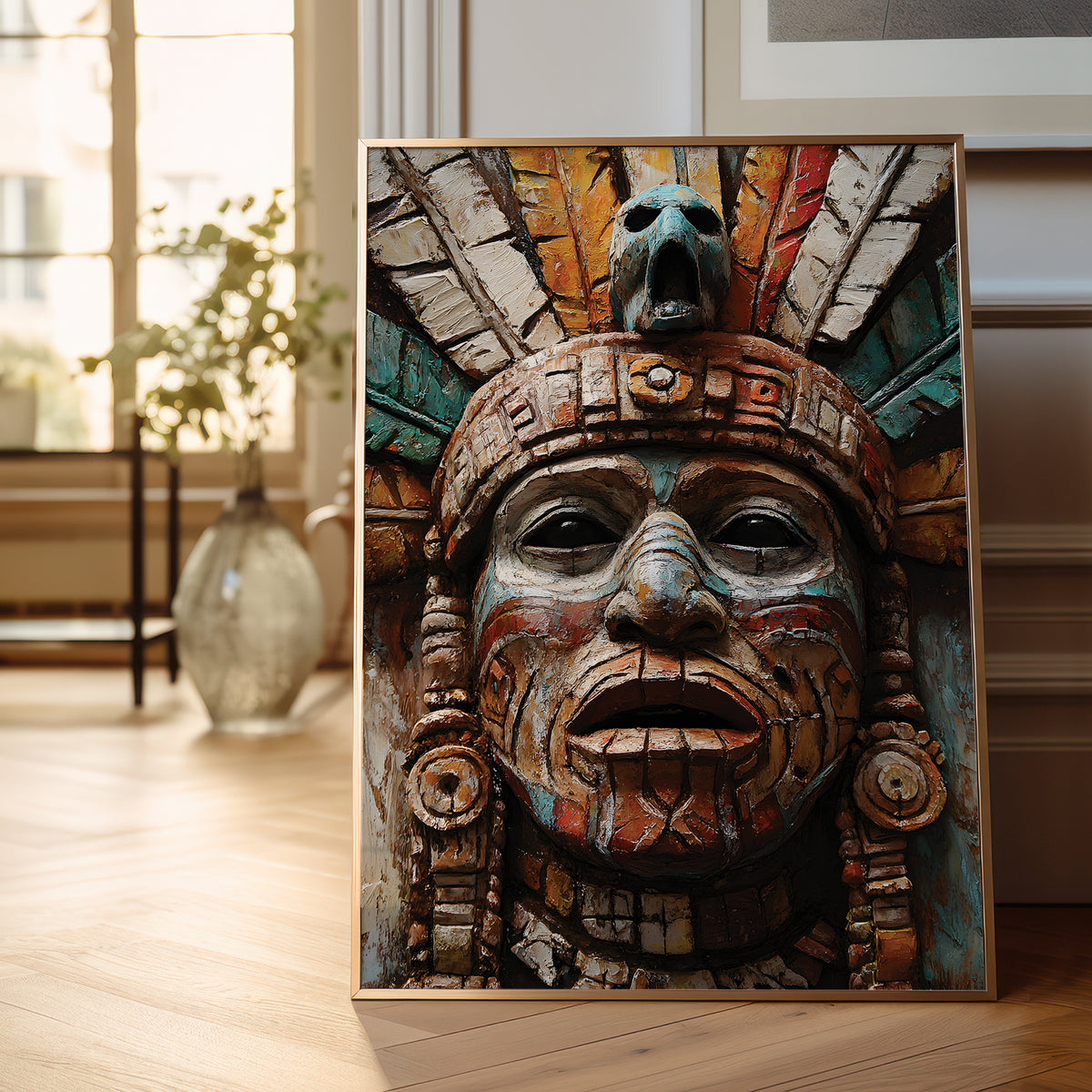 A framed art print depicting a detailed Aztec-style face with a feathered headdress, leaning against a wall on a light wood floor in a bright, modern room.
