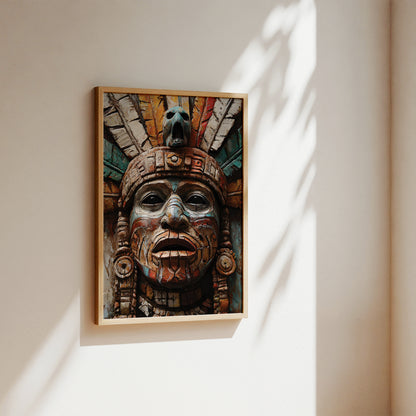 A framed art print featuring a detailed Aztec-style face sculpture with colorful painted details, hanging on a warm beige wall with soft sunlight and leaf shadows.
