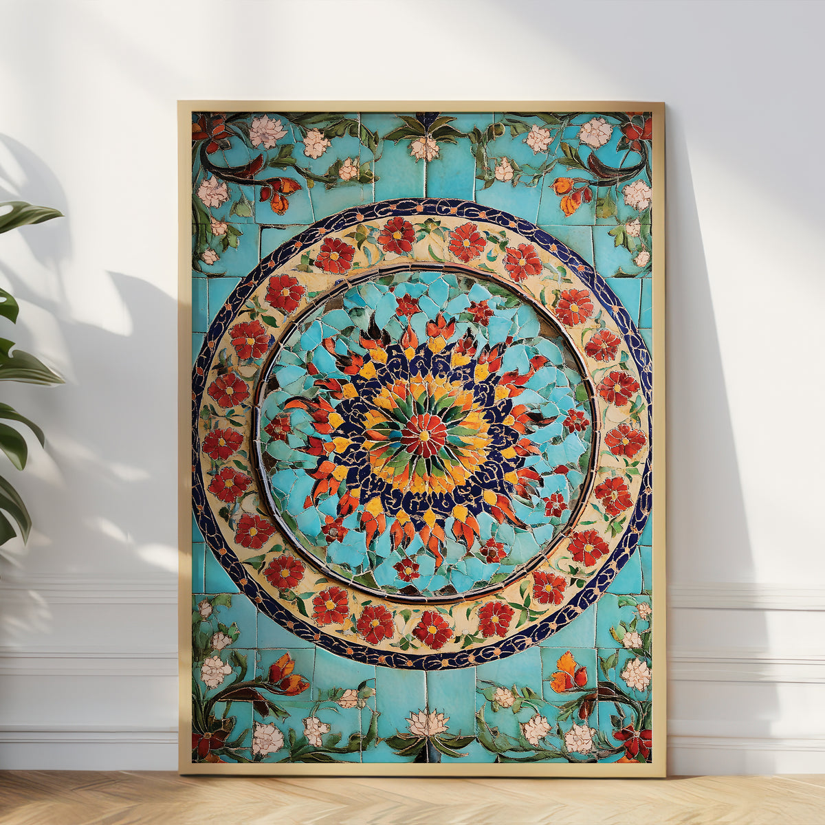 A large framed decorative tile wall art piece with a colorful floral mandala design, leaning against a white wall on a light wood floor next to a green plant.
