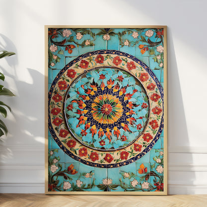 A large framed decorative tile wall art piece with a colorful floral mandala design, leaning against a white wall on a light wood floor next to a green plant.