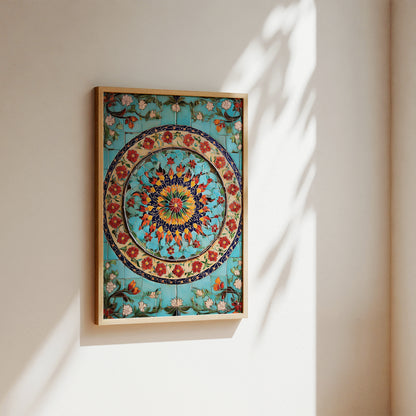 A framed square wall art print featuring a colorful circular floral mandala design on a turquoise background, hung on a beige wall with soft sunlight and leaf shadows.