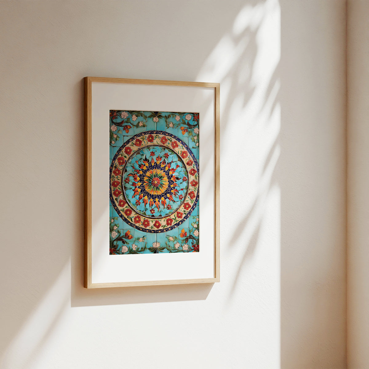 A framed art print featuring a colorful circular mandala design on a turquoise background, hanging on a beige wall with soft sunlight and leaf shadows.