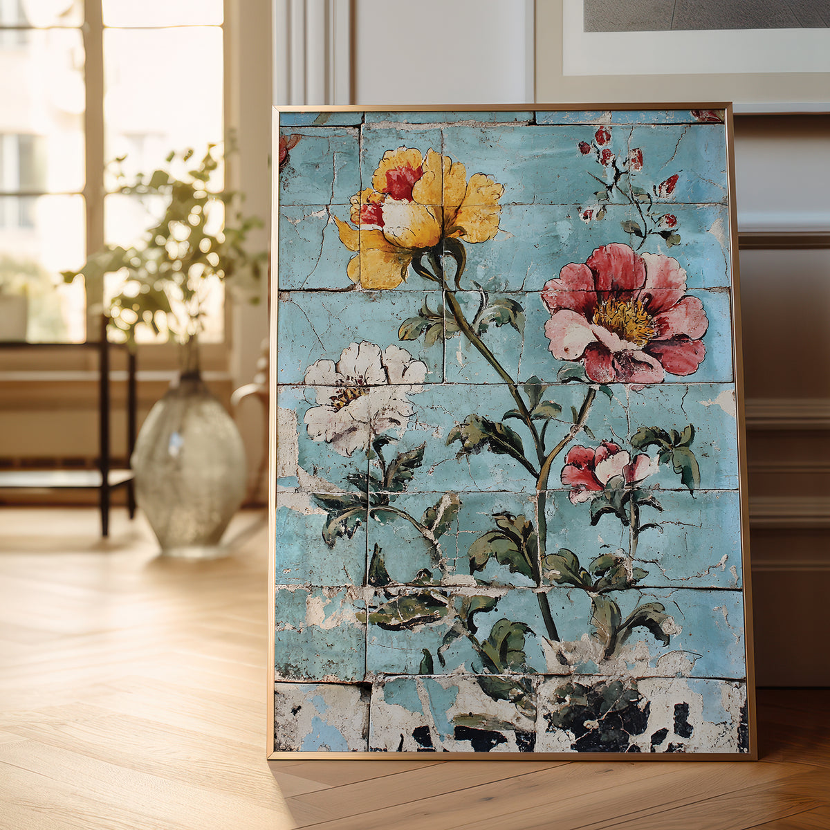 A framed floral art print leaning against a wall on a light wood floor. The artwork features large yellow, pink, and white flowers with green leaves over a distressed light blue wood-plank background.