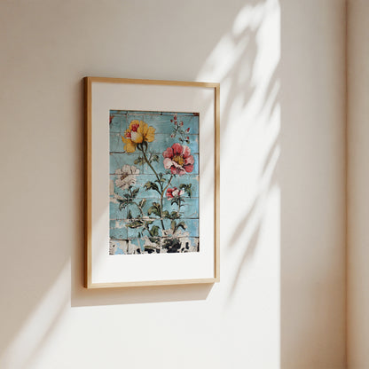 A framed floral art print with a light wood frame and white mat, hanging on a beige wall with soft sunlight and leaf shadows cast across it.