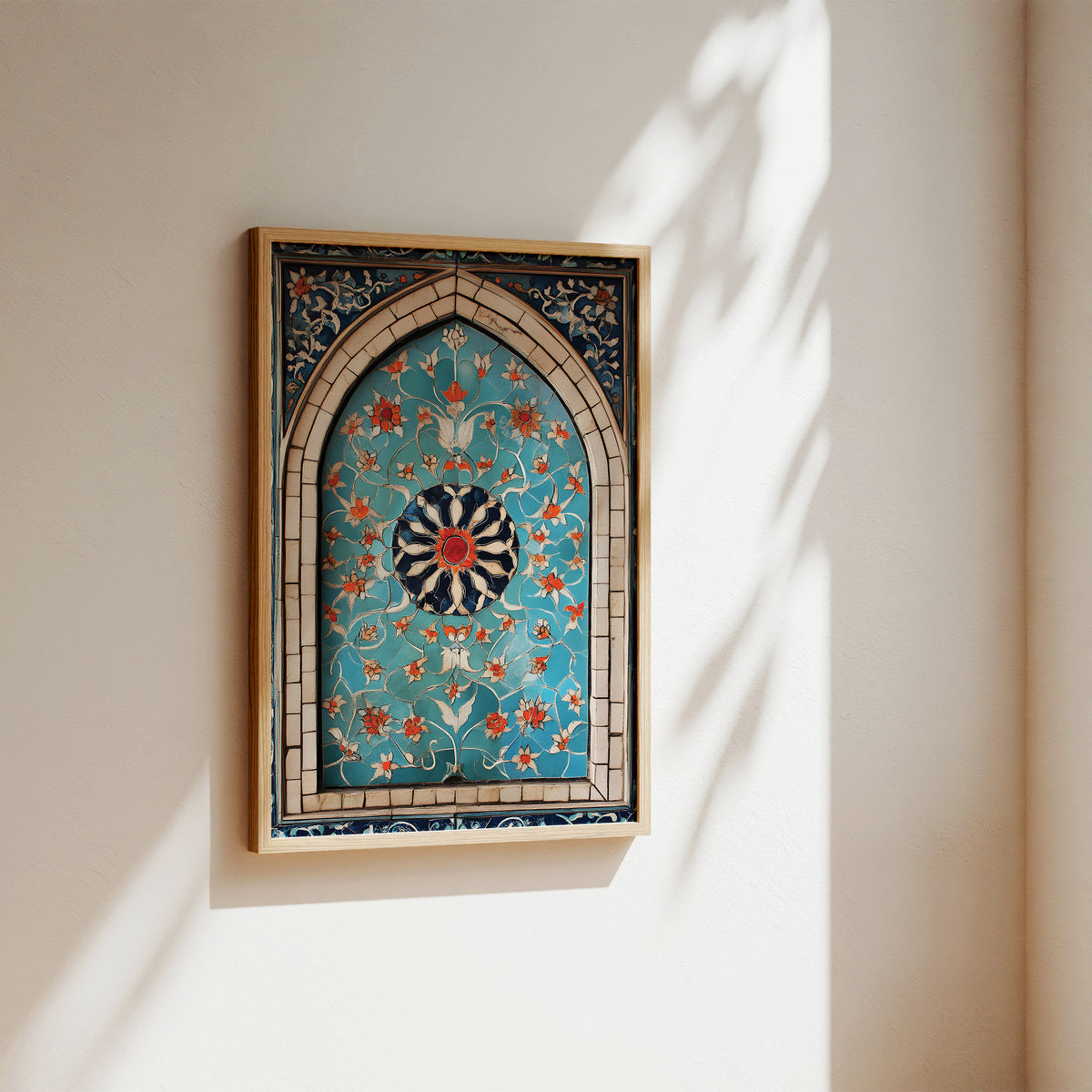 A framed Islamic wall art piece featuring an intricate turquoise, gold, and red floral pattern inside an arched tile design, hanging on a warm beige wall with soft sunlight and leaf shadows.