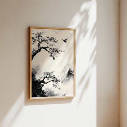 A framed wall art print featuring a black ink-style tree and bird scene on a warm off-white background, hung on a beige wall with soft sunlight and leaf shadows cast across it.