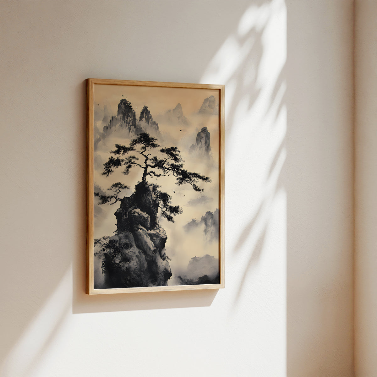 A framed vertical landscape art print featuring a dark pine tree on a rocky peak surrounded by misty mountains, hung on a warm beige wall with soft sunlight and leaf shadows cast across it.