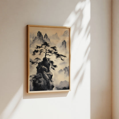 A framed vertical landscape art print featuring a dark pine tree on a rocky peak surrounded by misty mountains, hung on a warm beige wall with soft sunlight and leaf shadows cast across it.