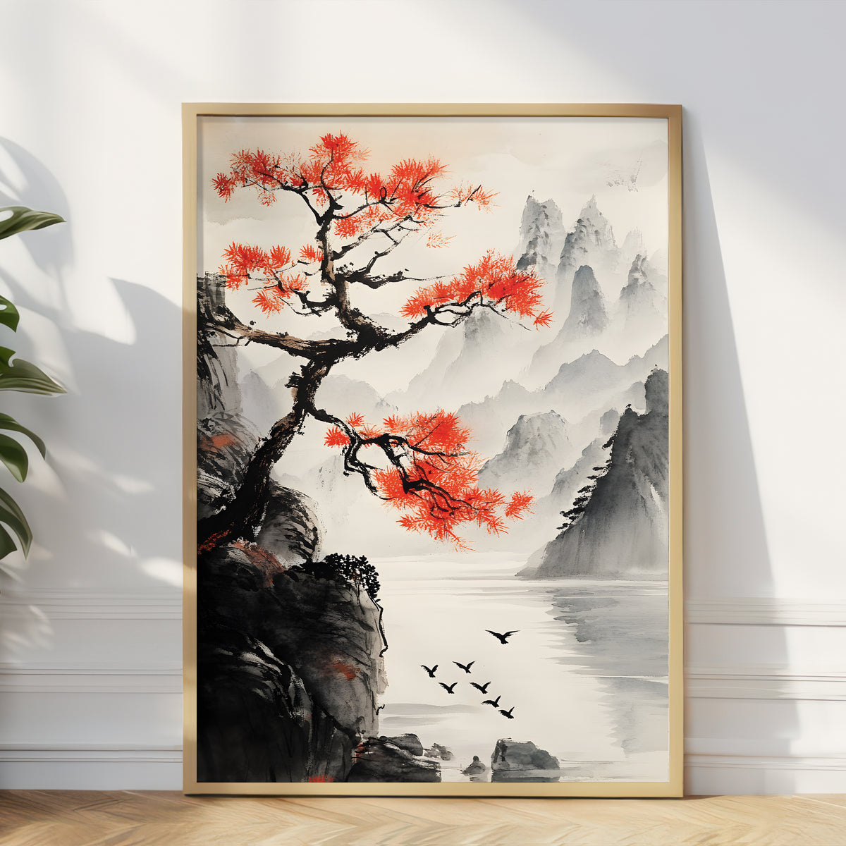 A framed vertical art print depicting a traditional Chinese landscape with a vibrant red tree, misty mountains, water, and birds, leaning against a white wall on a light wood floor.
