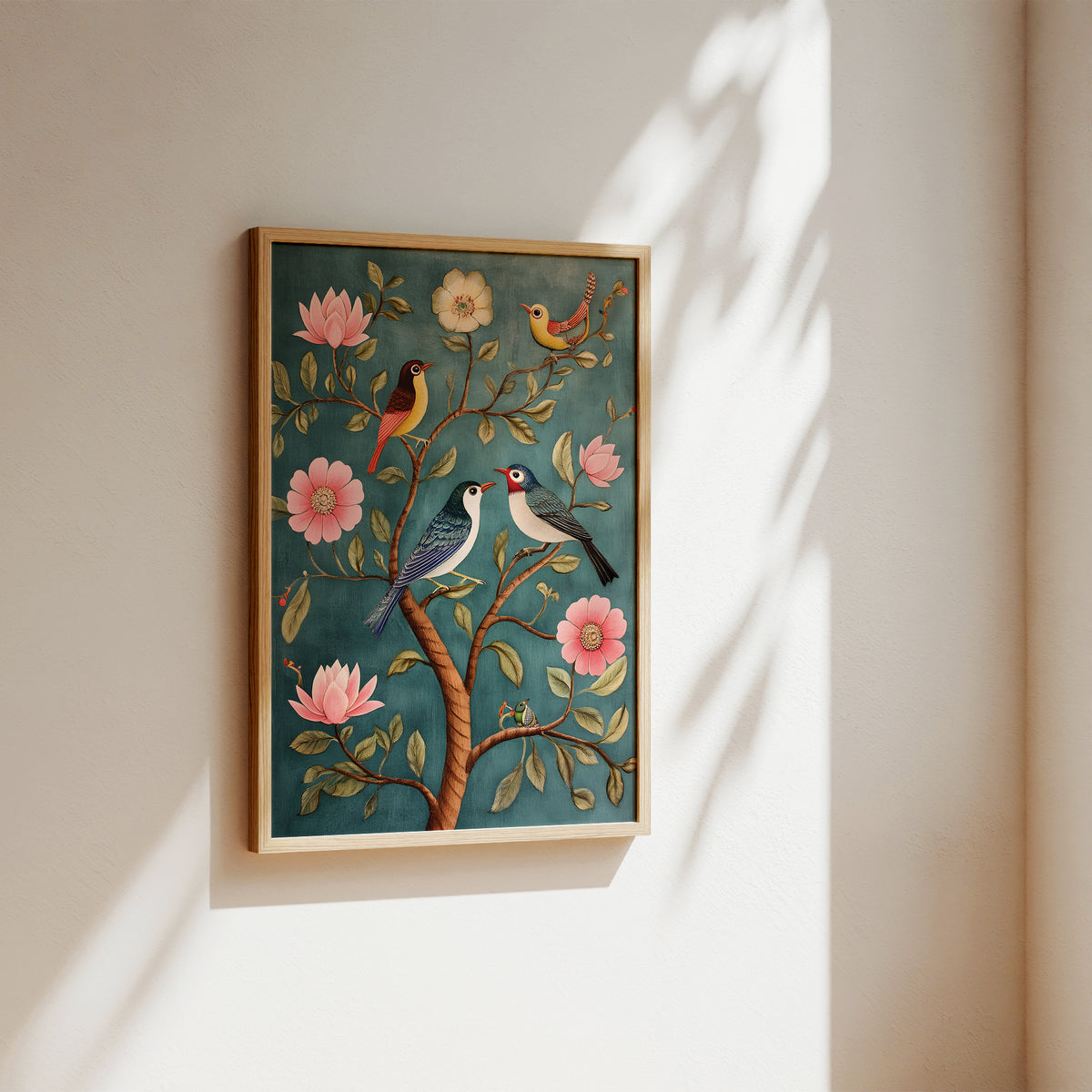 A framed wall art print featuring two birds perched on a tree with pink flowers and green leaves, displayed on a warm beige wall with soft sunlight and leaf shadows.