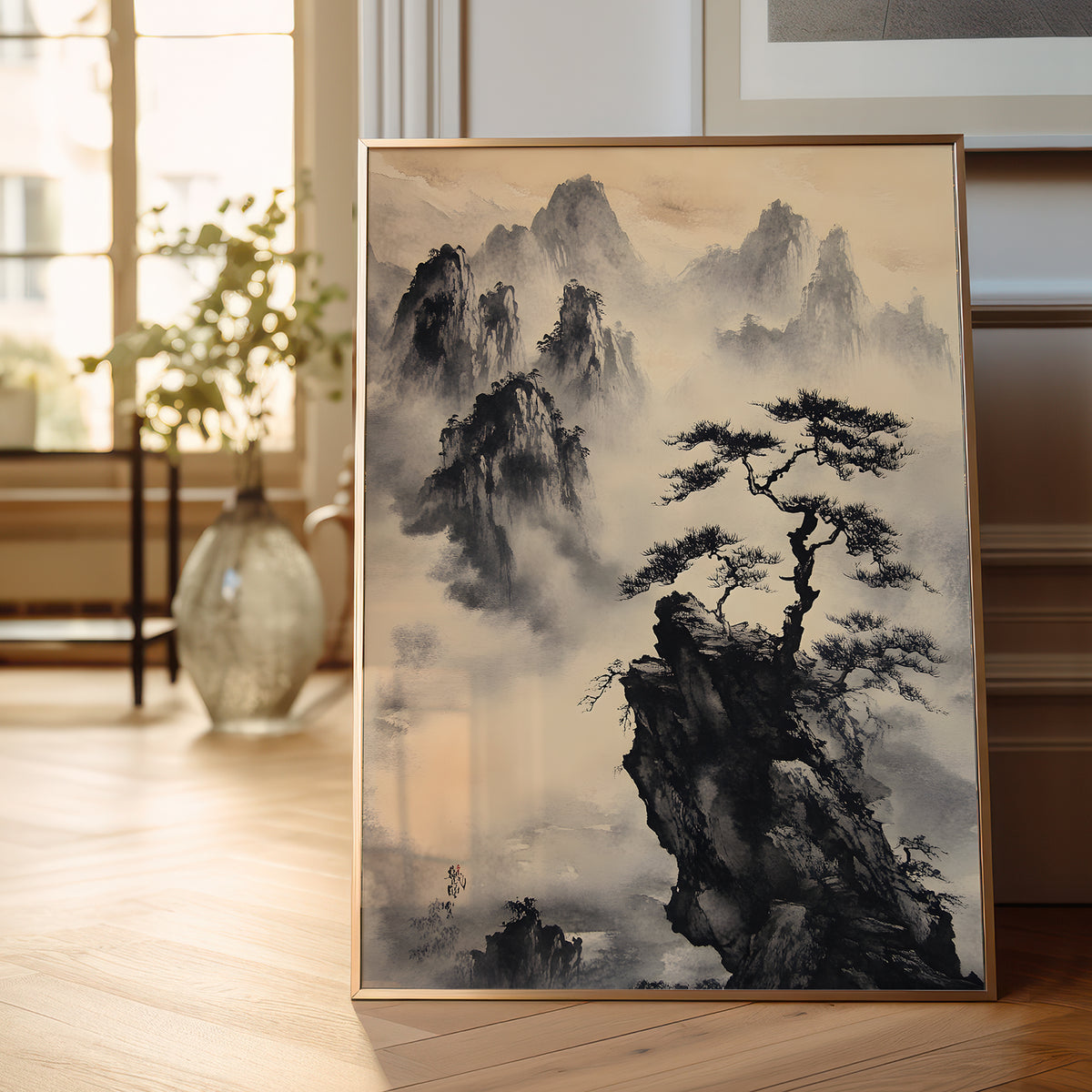 A framed vertical art print featuring a traditional Chinese ink painting of misty mountains and a lone pine tree, leaning against a wall on a light wood floor in a softly lit room.